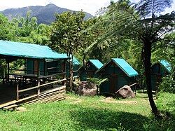 Several bungalows made of wood and blue-green tarp, along with a covered eating area.