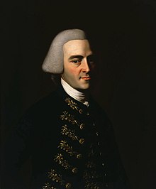 Half-length portrait of a man with a hint of a smile. His handsome features suggests that he is in his 30s, although he wears an off-white wig in the style of an English gentleman that makes him appear older. His dark suit has fancy embroidery.