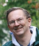 Head shot of a smiling man with glasses outdoors.