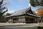 Wooden building with a hip-and-gable roof, an enclosing veranda and metal ornaments.