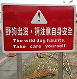 A sign reading "Stray dogs are nearby. Please be careful." in Chinese and English mistranslation "The wild dog haunts, take care yourself"