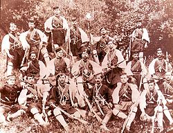 Black-and-white photo of a group of 18 armed men bearing weapons and bandoliers