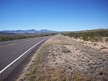 Image of FM 3078 passing through desert shrub land with the Davis Mountains looming in the distance.