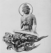 Front view of a seated statue with a ring-shaped halo. The figure is depicted playing a zither which is placed in front of it. The statue is positioned on a flower or cloud shaped pedestal.