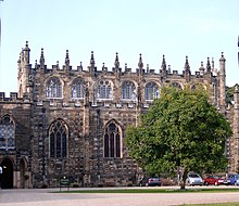 A two to three storey high stone building. The building is topped with castellations and pinnacles