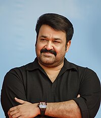 Mohanlal, wearing a black T-shirt, smiles with hands crossed, looking to one side