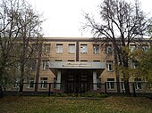 three story modern beige office building, gray portico with writing, trees, natural setting