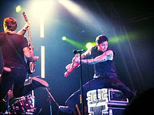 Two guys jumping with instruments in their hands