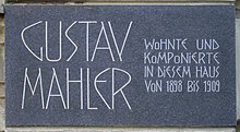 A dark plaque with white lettering in which the composer's name is shown in extra large characters on the left, the main message in smaller characters on the right