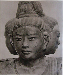 Portrait of a sculpture with three faces pointing to the front and both sides. Black and white photograph.