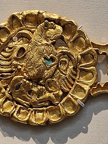 A Gold Parthian Belt Buckle, dated 1st to 3rd century AD, with an eagle in the centre holding a sheep or goat. On the left-hand side of the eagle's Brest is what appears to be a heart symbol. There is either pigment or a stone inlaid inside the heart symbol.