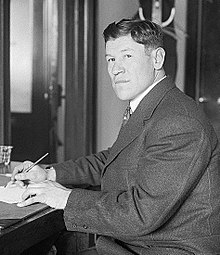 Black-and-white image of Jim Thorpe sitting down and writing. He is an Native American man with a Western haircut and wearing a dark suit.