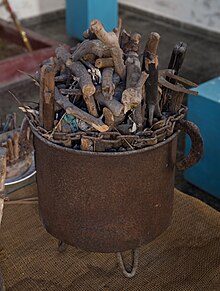 A small iron cauldron packed with sticks; a small chain is tied around it.