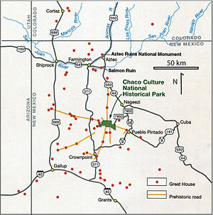 Large square map of northwestern New Mexico and neighboring parts of, clockwise from left, western Arizona, southeastern Utah, and southwestern Colorado. The map region has a green and blocky rectangular-crescent area at its center labeled Chaco Culture National Historical Park. Radiating from the green region are seven segmented gold lines: "[p]rehistoric roads", each several dozen kilometers in length when measured according to the map scale factor. Roughly seventy red dots mark the location of great house[s]; they are widely spread across the map, many of them far from the green area, near the extremes of the map, more than one hundred kilometers from the green area. Two proceed roughly south, one southwest, one northwest, one straight north, and the last to the southeast. Yellow dots mark the location of modern settlements: Shiprock, Cortez, Farmington, and Aztec to the northwest and north; Nageezi, Cuba, and Pueblo Pintado to the northeast and east; Grants, Crownpoint, and Gallup to the south and southwest. They are connected by a network of gray lines marking various interstate and state highways. A fan of thin blue lines along the northern margins of the map depict the San Juan River and its communicants.