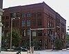 =A large four-story red brick building with many windows. The building is on a street corner with the front and one of the sides visible.