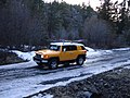 A Sun Fusion Yellow Toyota FJ Cruiser with optional equipment negotiating some snowy terrain.