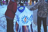 "A colour photograph of a young girl in a traditional shawl between two adults"