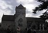 Gray stone building with arched windows. A central tower has a clock on the near face and is surmounted by a weather vane.