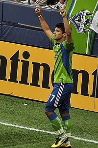 A man in a footballer's uniform raising his hands in the air.