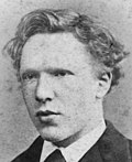 Headshot photo of the artist as a cleanshaven young man. He has thick, ill-kempt, wavy hair, a high forehead, and deep-set eyes with a wary, watchful expression.