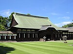 Wooden building with a hip-and-gable roof and attached canopy with Chinese style gable. On either side, the building is connected to a wooden corridor.