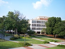 A sidewalk surrounded by landscaped green space in the foreground with a four-story white concrete building in the background