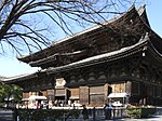 Large wooden building with a hip-and-gable roof and enclosing pent roof.