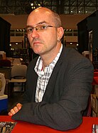 A suited bald man looks directly into camera at a signing event.