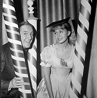 publicity shot of elderly man and young female sitting between three poles