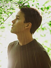 Justin Nozuka from profile, wearing an olive-green sweater, looking up slightly, with lips parted