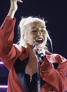 A blond woman singing while handling a microphone