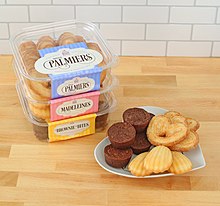 Boxes of palmier cookies stacked on top of each other next to heart shaped plate of palmiers and brownies