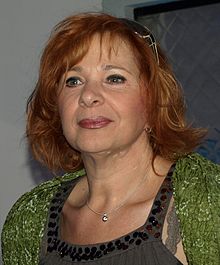 close-up of Kamila Magálová wearing a green top over a grey sleeveless top, looking right of camera with slight smile