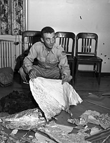 Marcel holding torn foil above packing paper