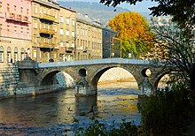 Latin bridge (prev. Princip bridge) in Sarajevo. Across the bridge is a street of several grayish houses not more than four stories high.