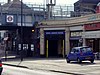 A beige building with a rectangular, dark blue sign reading "NORTH HARROW STATION" in white letters all under a light blue sky with white clouds