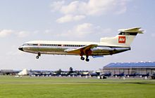 A jet airliner with the letters 'BEA' on the tail fin flies close to the ground from right to left with its undercarriage extended.