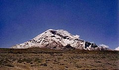 A snow-capped mountain lies in the distance against a cloudless blue sky. The land in the foreground is very barren.