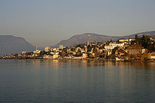 A collection of houses and other small buildings scatter the shore of a wide lake