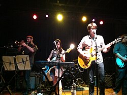 Two guys and a girl playing guitar and another guy playing a trumpet