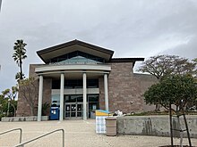 A tall brown brick building with a glass upper level, and white columns