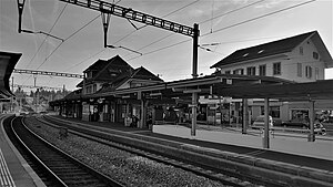 Three-story hip-roofed building next to double-track railway line with canopy-covered side platforms