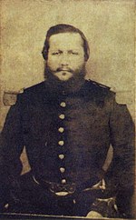 Head and torso of a large bearded man wearing military clothing.