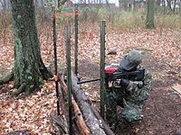 A woodsball player firing at opponents from behind cover. Note the stock and sights for woodsball style play.