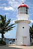 A white conical lighthouse with a lantern, double gallery, and red dome