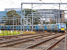 A long train arriving into Dandenong station, with 4 tracks, signalling, and electrical equipment shown