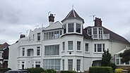 A large white house, partly with pitched roofs, and one section being surmounted by a tower-like structure with windows set in