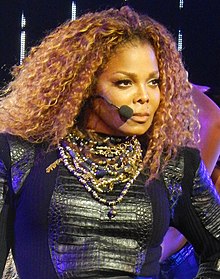 Janet Jackson, on stage, with big curly hair looking to her left