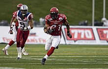 Two football players running on a green field.