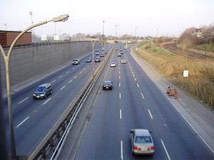 8-lane roadway from an overhead bridge with parallel 3 lines of train tracks on the right